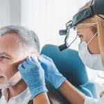 Senior patient with hearing loss getting his ears examined by a medical professional.