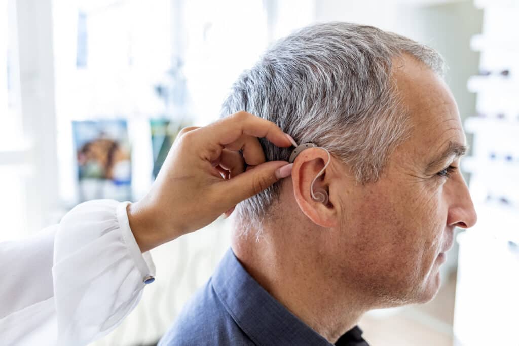 Audiologist positioning a man's hearing aid.
