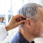 Audiologist positioning a man's hearing aid