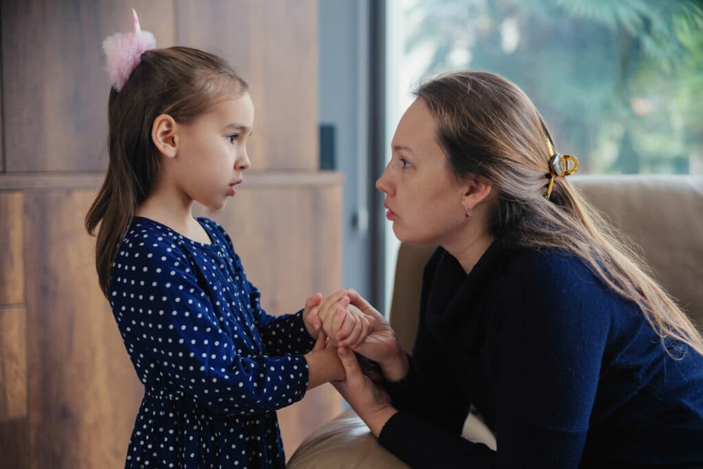 Young mom talking to her daughter, holding her hand.