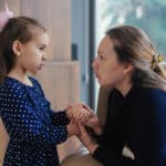 Young mom talking to her daughter, holding her hand