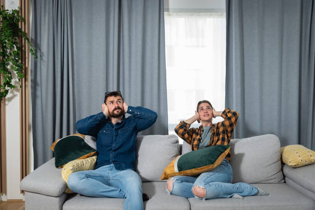 Two people in their home cover their ears.