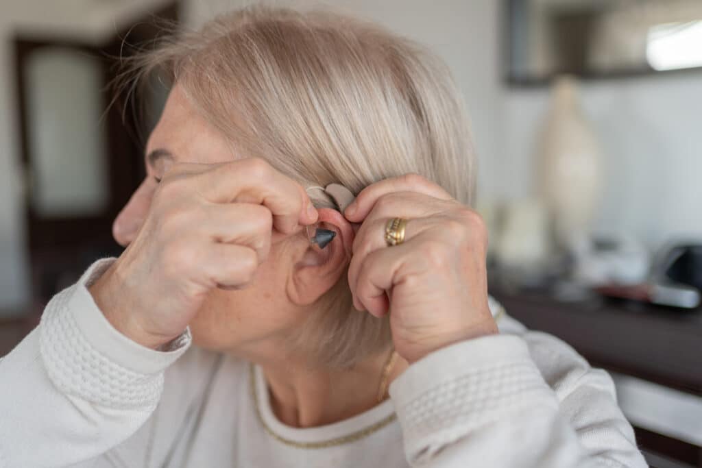Senior woman holding a hearing aid up to her ear.