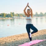 Senior woman practicing yoga tree pose on lake shore